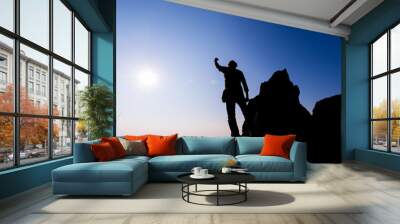 Silhouette of people Hike on the peak of rocks mountain at sunset with arms raised up above head in celebration Wall mural