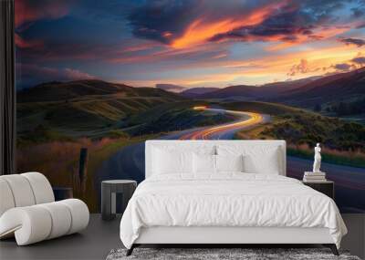 Scenic winding road through rolling hills at sunset with stunning sky, showcasing motion blur of car lights emphasizing travel and adventure. Wall mural