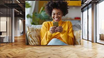 Excited happy young black woman holding smart phone device sitting on sofa at home - Happy satisfied female looking at mobile smartphone screen gesturing yes with clenched fist - Technology concept Wall mural