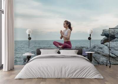 Side view of woman doing exercise yoga. sitting in Sukhasana exercise, Easy Seat pose pose. Amazing yoga landscape in beautiful and enjoying sea view with evening, concept for exercising, health care Wall mural