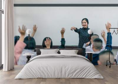 A smiling Asian female high school teacher teaches the white uniform students in the classroom by asking questions and then the students raise their hands for answers. Wall mural