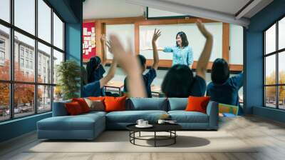 An smiling Asian female high school teacher teaches the blue uniform students in the classroom by asking questions and then the students raise their hands for answers. Wall mural