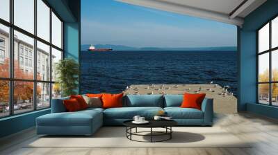 Gray seagulls sit on a concrete dock against the backdrop of the blue sea, mountains and a passing red ship. Wall mural