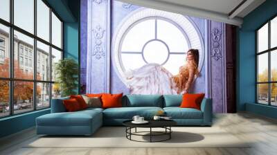 Charming girl with makeup in luxurious dress with feathers, lies on round window Wall mural