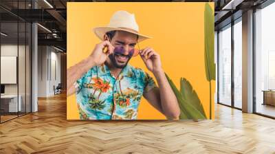 handsome Latino American young man in summer clothes and with sunglasses winking orange background with a plant medium closeup studio shot summer concept. High quality photo Wall mural