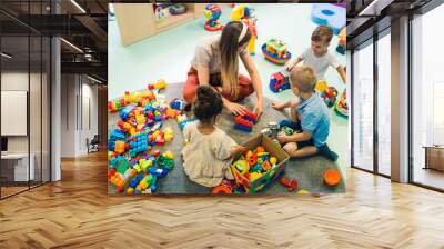 Playtime at nursery school. Toddlers with their teacher sitting on the floor and playing with building blocks, colorful cars and other toys. High quality photo Wall mural