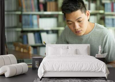 male asian student studying and reading book in library Wall mural