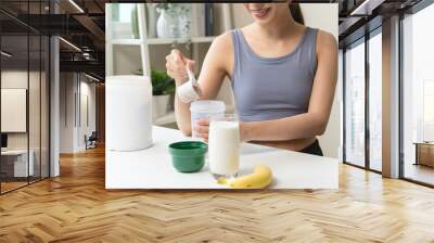 Young sporty woman pouring protein powder into a cup to make replacement food meal after workout Wall mural