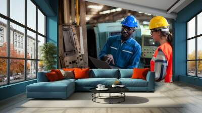 African Technician operator machine and Caucasian woman  programmer engineer are working in factory, checking lathe machinery operating with laptop to maintain safety of work, Safety first concept. Wall mural