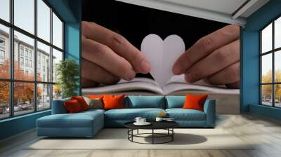 Book with open pages and heart shaped paper. Woman hand holding heart shaped paper over open book on table. love of reading concept Wall mural