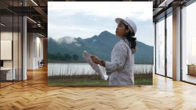 Engineering ecologist woman in a helmet holding a blueprint stands on the bank of a river to develop a hydroelectric dam to generate electricity. Clean energy and Technology concepts. Wall mural