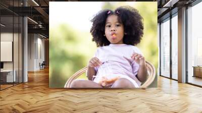 Cute afro curly girl Girl sitting eating sausage in the lawn. Wall mural