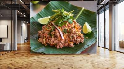 A close-up of a delicious Thai dish with minced meat, vegetables, and lime wedges on a banana leaf. Wall mural