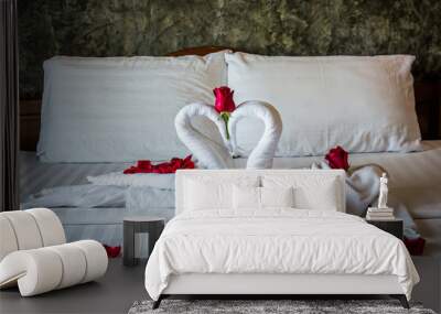 Two swans on a bed rolled from towels on a white bed with red roses specially decorated for honeymoon and valentines day in hotel. Wall mural