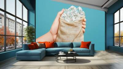 A hand holding a bag filled with sparkling diamonds against a blue background, symbolizing wealth and luxury. Wall mural