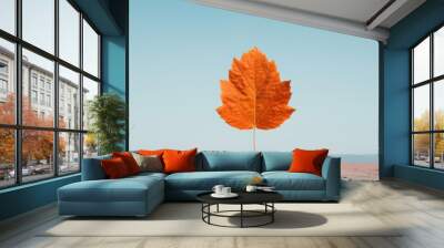 A vibrant orange leaf floating against a serene blue sky, capturing the beauty of autumn in a minimalist composition. Wall mural