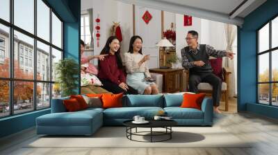 asian family laughing and pointing with finger enjoying watching tv together in living room on chinese lunar new year holiday. word at background translation: spring and congratulation Wall mural