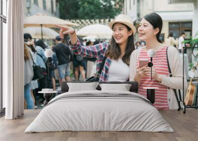 asian girl friends at farmer market outdoors in summer in city. two young female travelers holding cellphone with map online app searching and point finger while find shop destination tokyo japan Wall mural