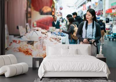 asian woman traveler with camera passing by a local stall selling Japanese processed seafood while visiting kuromon ichiba market in Osaka japan Wall mural