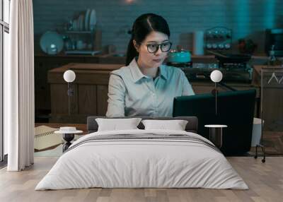 Attractive young asian chinese woman working in home kitchen at night. office lady using laptop computer in dark workplace in midnight. concentrated female worker in glasses using notebook pc. Wall mural