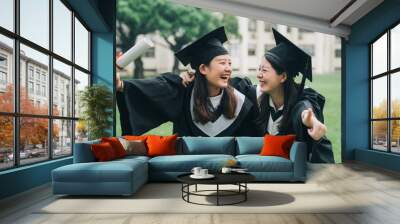 Graduation asian female friends hold diploma. cheerful ladies students hugging shoulders arms with thumb up finger hand gesture best sign. beautiful cheerful women students looking each other smiling Wall mural