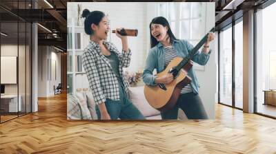 Group of asian female friends playing karaoke at home. Concept about friendship home entertainment young people. two girl roommates love music happy relax dancing singing with bottle of beer. Wall mural