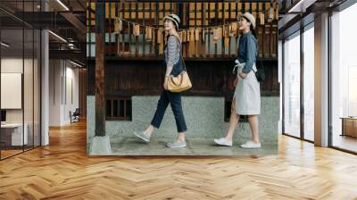 side view full length two asian women tourist visiting in japanese style wooden house with zen garden looking up enjoy nature spring view. young girls friends walk in walkway by wood hope cards wall Wall mural