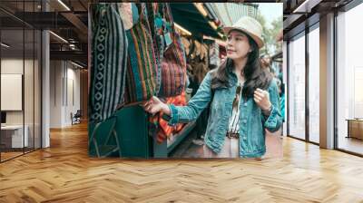 Summer holidays shopping concept. Young asian woman tourist buying souvenirs in gift olvera street stall outdoor picking choosing bags at vendor. girl traveler shopping in mexico market on sunny day Wall mural