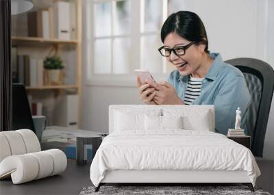 Surprised young female student chatting with best friends in social network on mobile phone while received shocking good news. cheerful college girl relax using cellphone while doing homework at home Wall mural