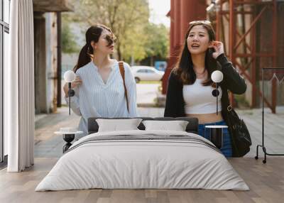 Two asian japanese female friends relax walking outdoors together in red old factory. group of young beautiful girls tourists sightseeing in historic tourism attraction on sunny day in summer time. Wall mural