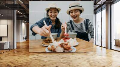 two happy smiling asian girls travelers love delicious food trying taiwanese local meal sitting in vendor traditional restaurant shop store. young women cheerful using chopsticks ready to eat. Wall mural