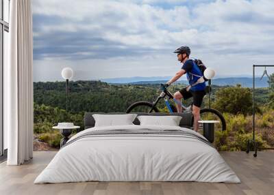 Male mountain biker on ebike standing on top of a hill, looking left Wall mural