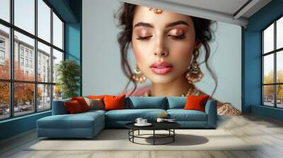 A stunning portrait of a beautiful Indian woman wearing ethnic clothing and traditional jewelry, featuring pastel pink lips and brown eye shadow against a grey background Wall mural