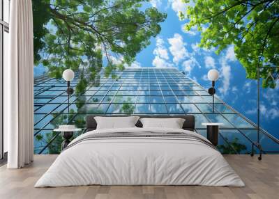 Sustainable architecture exterior view featuring a green building concept with a glass curtain wall, set against a backdrop of green trees and a blue sky. Wall mural