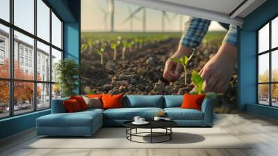 A single person standing near young plants growing from rich soil, with wind turbines towering in the background, symbolizing a commitment to green energy and sustainability Wall mural