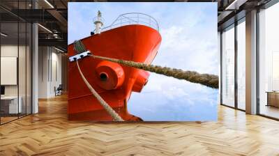 Low angle view of cargo ship docked at port with mooring rope against white clouds on blue sky background Wall mural