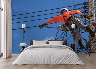 Low angle view of electrician with safety equipment and various work tools is installing cable lines and electrical system on electric power pole against blue sky background Wall mural