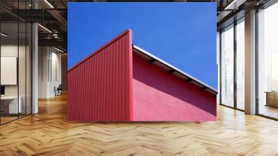 Low angle view of empty red corrugated steel wall decoration on pink wall of modern building against blue clear sky background Wall mural