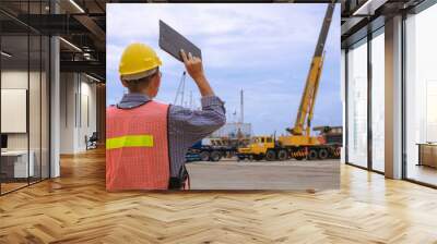 Rear view of Asian foreman in reflective clothing with safety helmet is working to transferring cargo from barge into trailer truck in shipping port Wall mural