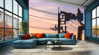 Silhouette of 2 electricians on bucket boom truck are repairing electrical system on electric power pole against sunset sky background in evening time Wall mural