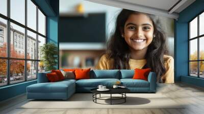 Indian teen girl sit on the couch playing video game console, she is holding gamepad, happy expression. Wall mural