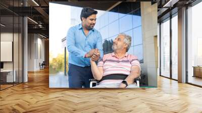 Young man giving support to sick old man in a wheel chair. Wall mural