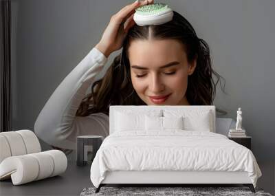 Beautiful young woman using hair scalp massager on grey background Wall mural