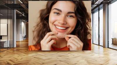 Close up cropped young woman wear orange shirt casual clothes hold in hand invisible transparent aligners, invisalign bracer smile isolated on plain pastel light beige background. Lifestyle concept. Wall mural