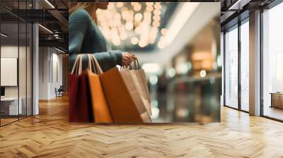 Close-up of unrecognizable woman in casual clothing standing in spacious shopping mall with lights and holding many paper bags Wall mural