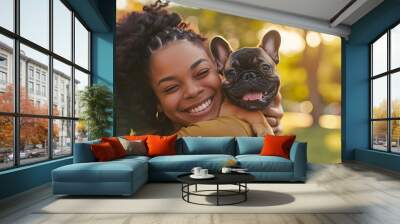 Happy mixed race woman cuddling French bulldog dog in the park, copy space AI Wall mural