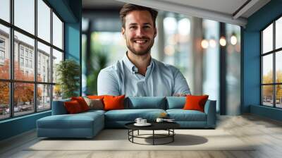 Portrait of cheerful businessman with arms folded standing in conference room. Happy young business man in shirt looking at camera. Portrait of a smiling businessman in modern office Wall mural