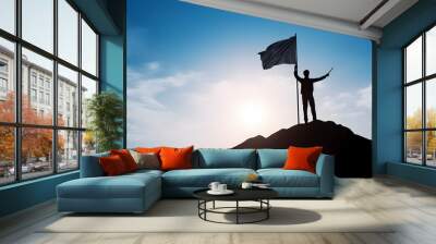 Silhouette of businessman holding flag on the top of mountain with over blue sky and sunlight. It is symbol of leadership successful achievement with goal and objective target. Wall mural