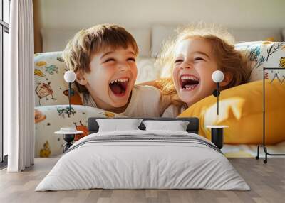 Two young children playfully laugh while resting on a bed surrounded by bright pillows, enjoying a fun and lively moment together in a cozy, sunlit room Wall mural