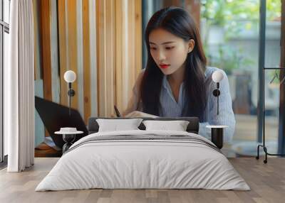 Young asian businesswoman checking marketing data of business on document and typing data on keyboard laptop while thinking about investment and planning of new startup project for working in cafe Wall mural